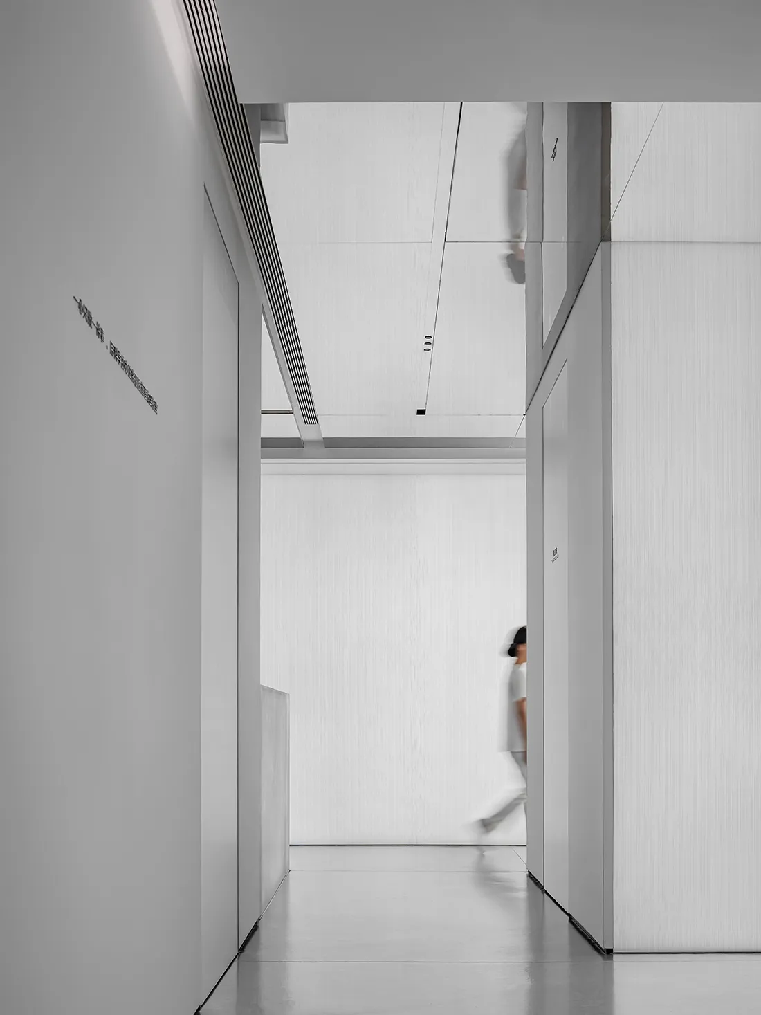 A minimalist white interior featuring a corridor with white walls and floor, leading to a white-walled room.