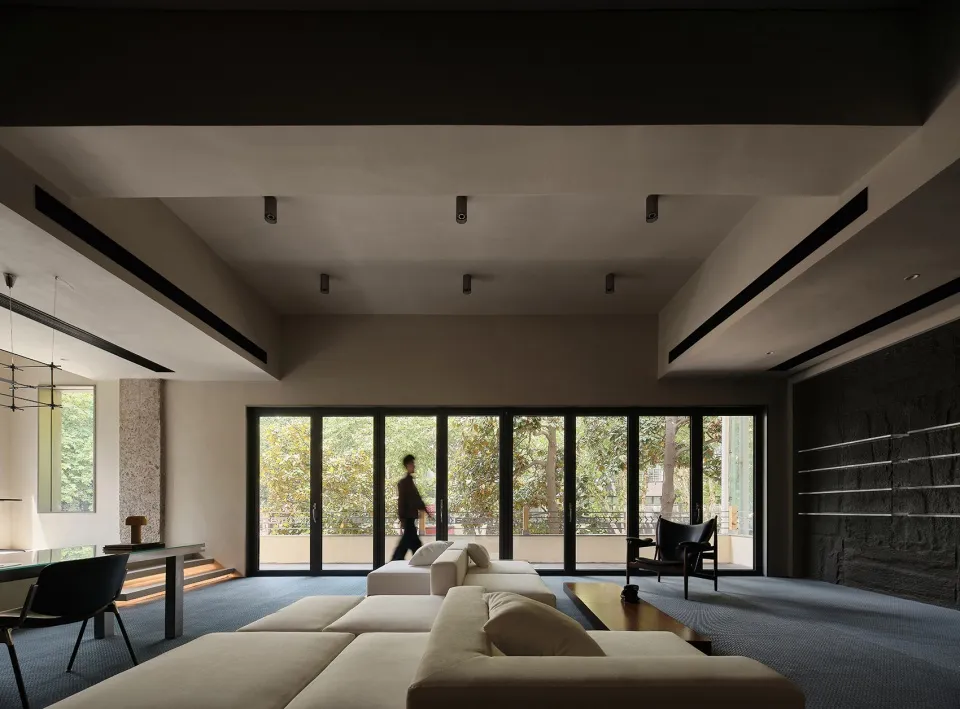A modern living room featuring a taupe-colored sofa and upholstered furniture, large floor-to-ceiling windows, and a minimali