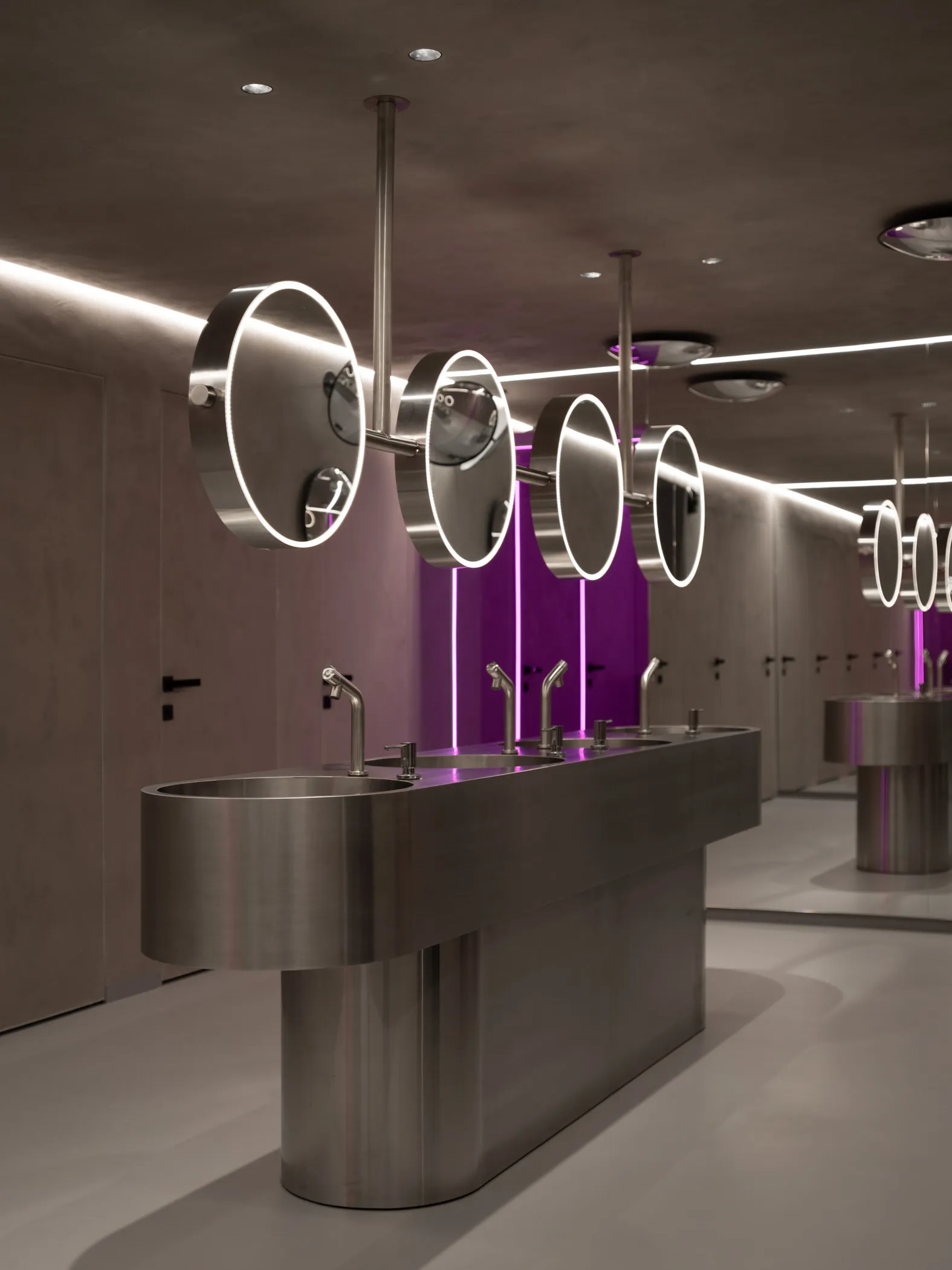 Modern public restroom with metal sinks and glass stalls