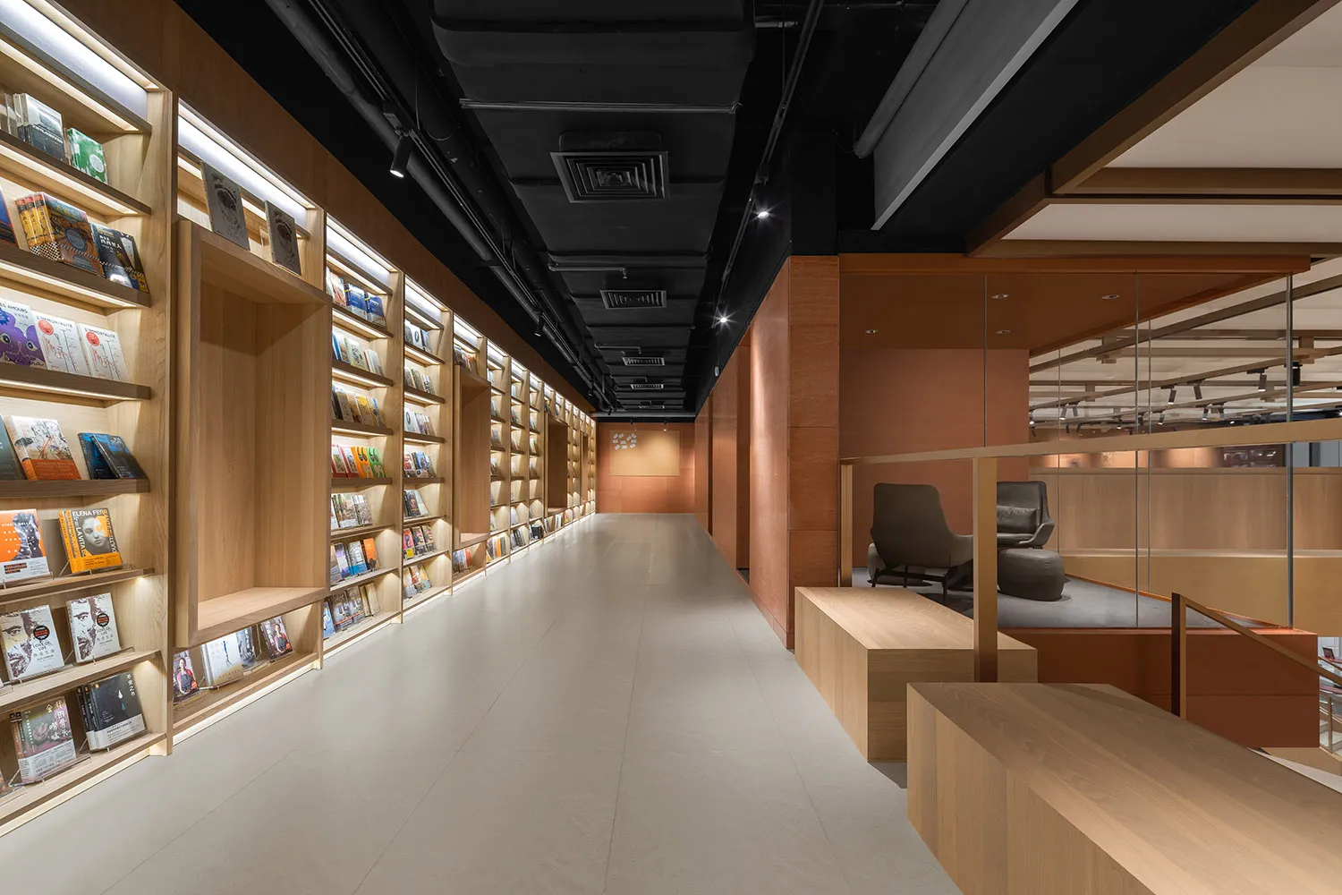 A modern library with wooden shelves, illuminated by LED lights, featuring a mix of books and magazines, and a seating area w