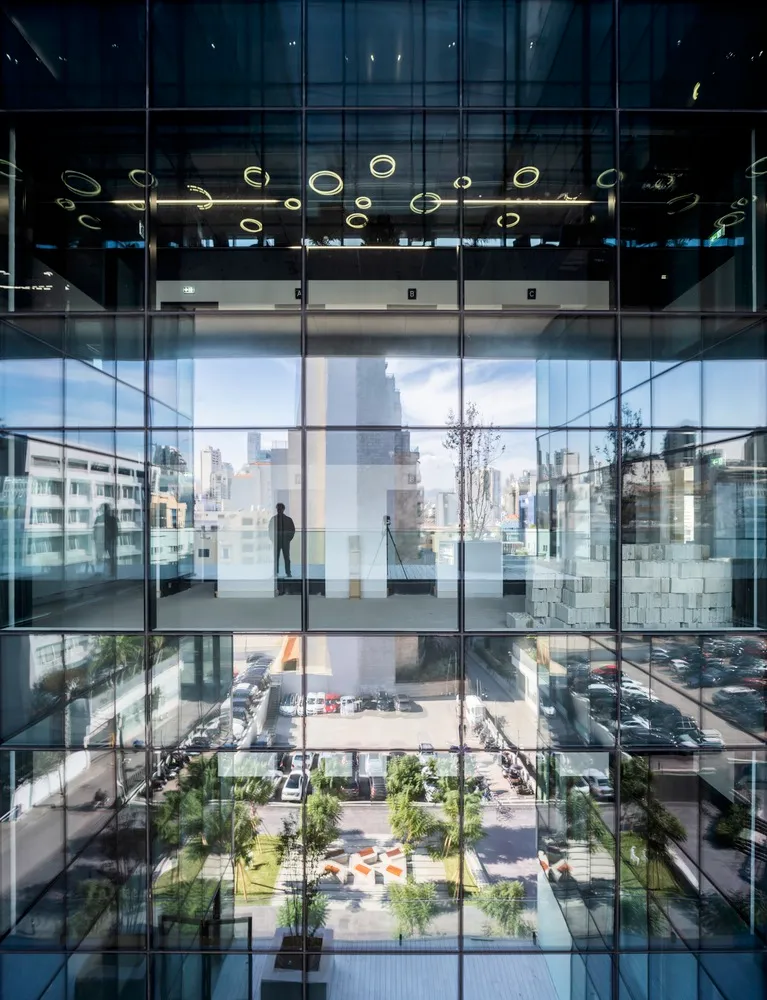 A modern office building with a glass facade viewed from the street level, reflecting the cityscape.