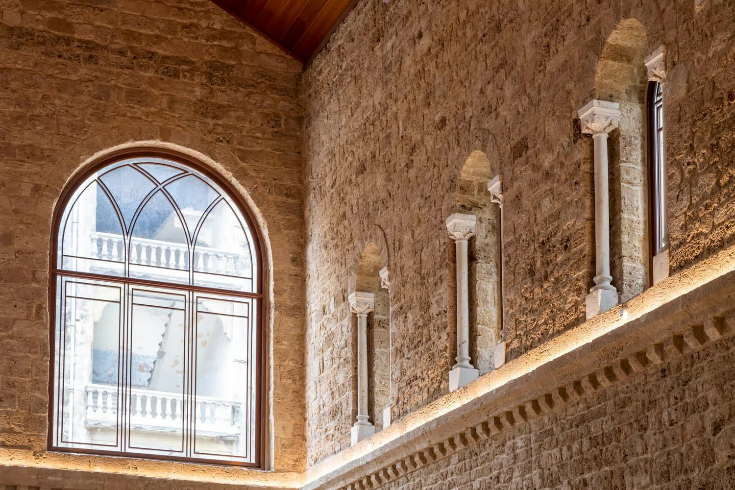 A modern interior space with a stone wall featuring a large, arched window.