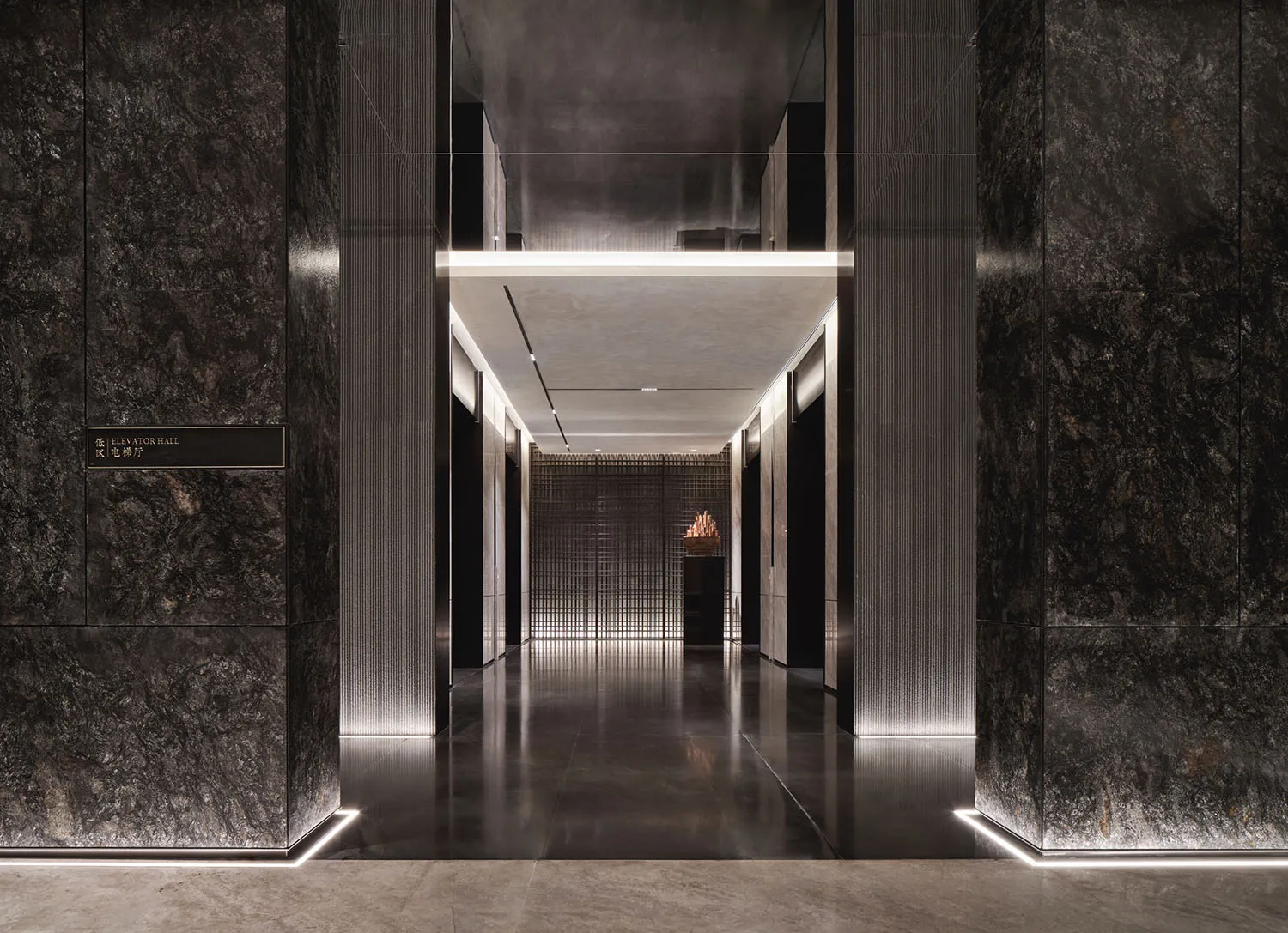 A modern corridor with dark marble walls, illuminated by subtle lighting, leading to a lobby area.