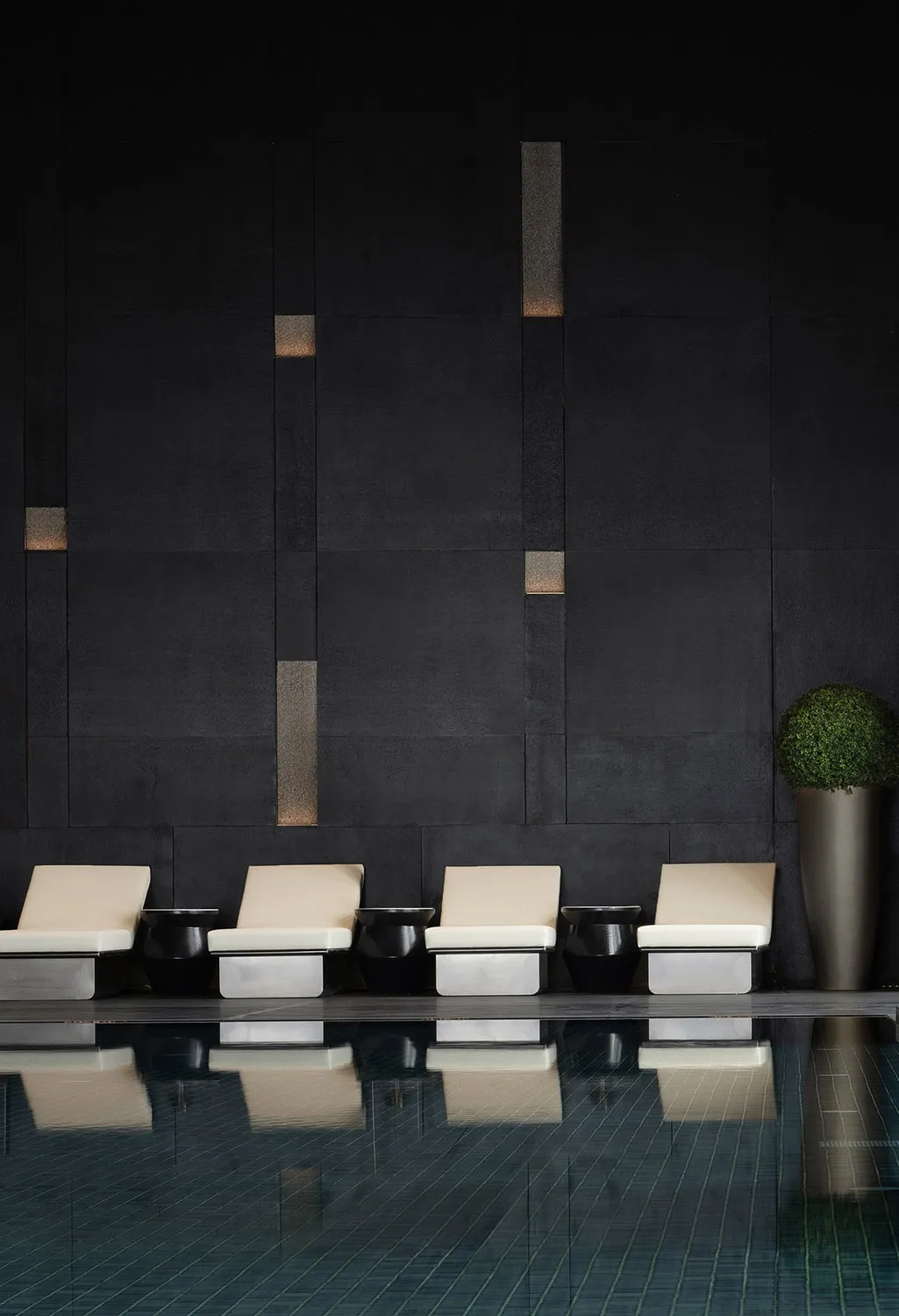 A modern poolside lounge featuring concrete seating and lighting.