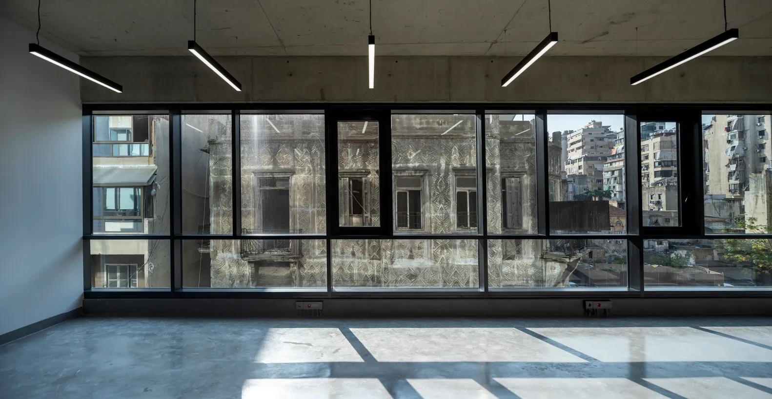 A spacious, empty interior space featuring large glass windows reflecting an urban cityscape.