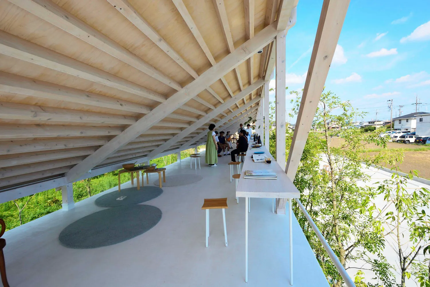 現代建築室內空間,搭配木質天花板,設有長桌與座椅,周圍環繞樹木與開闊天空。