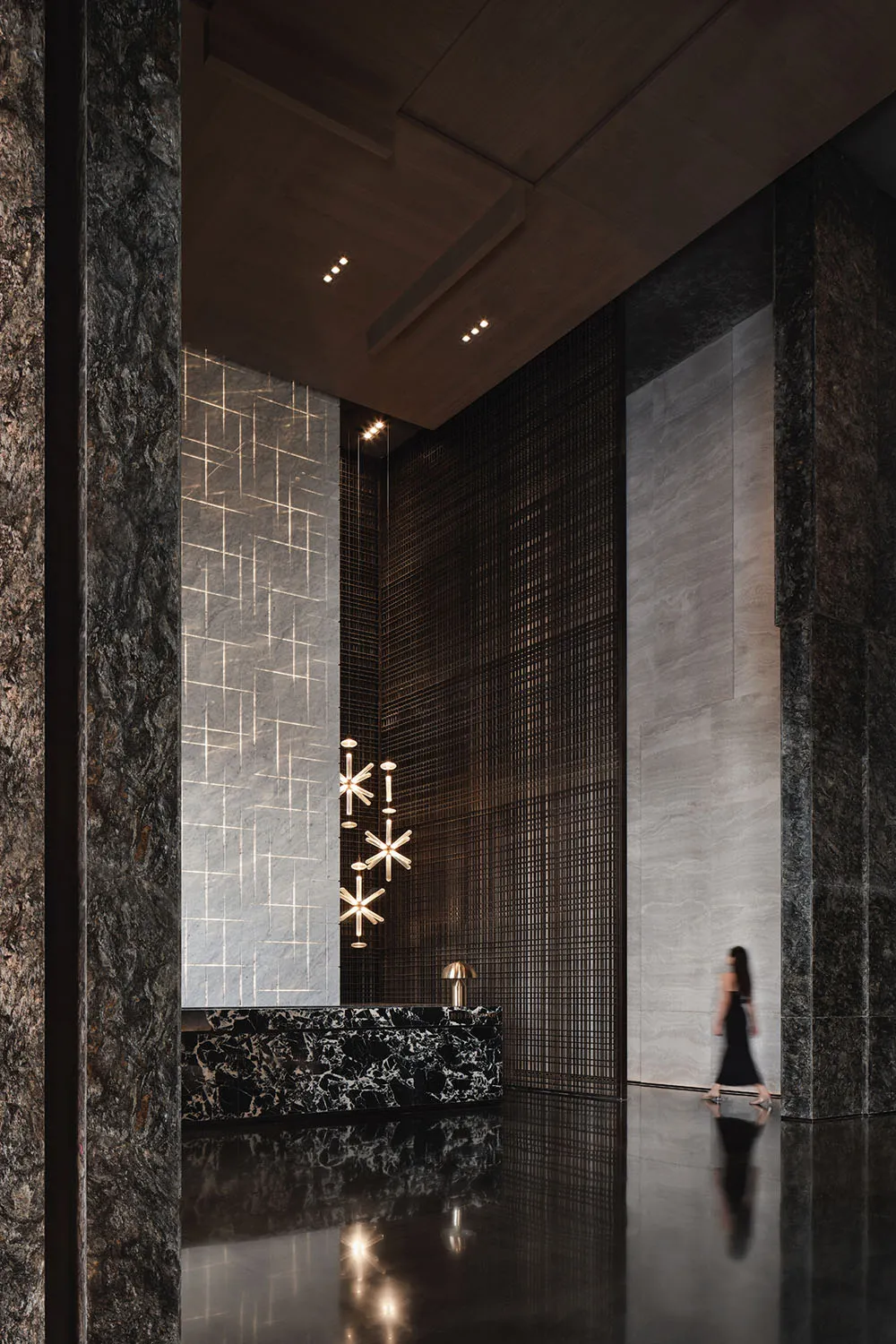A spacious modern minimalist lobby with marble walls and floors, featuring geometric lighting fixtures and a sleek black rece