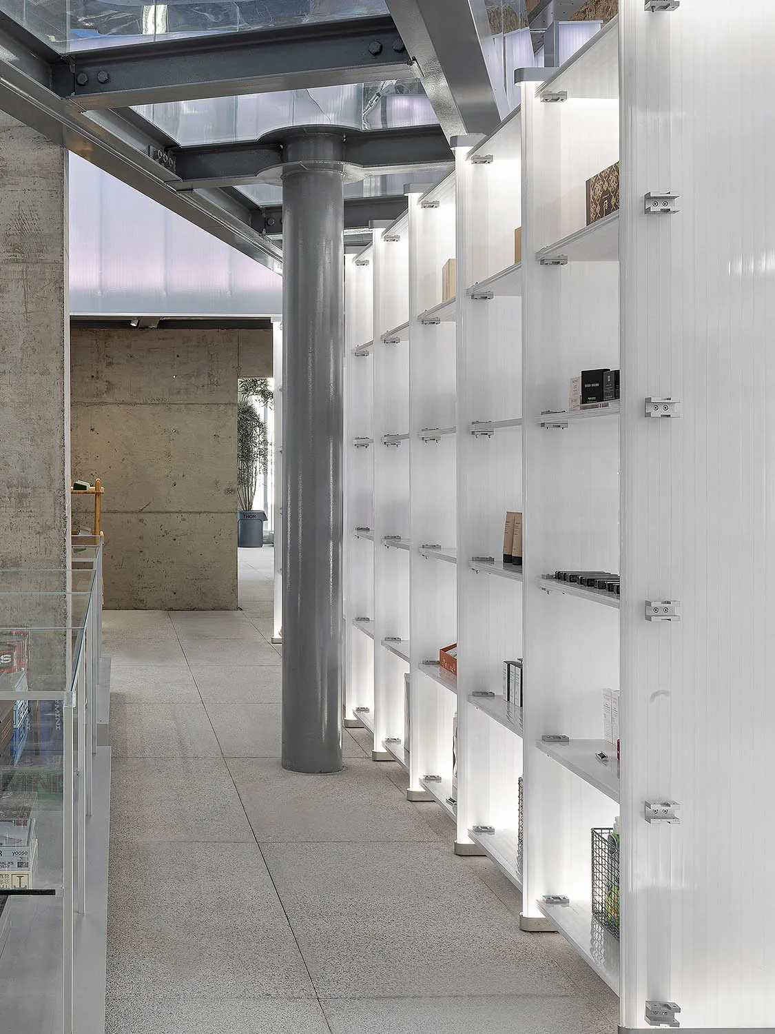 Modern shop interior showcasing white shelves against concrete pillars and a glass ceiling.