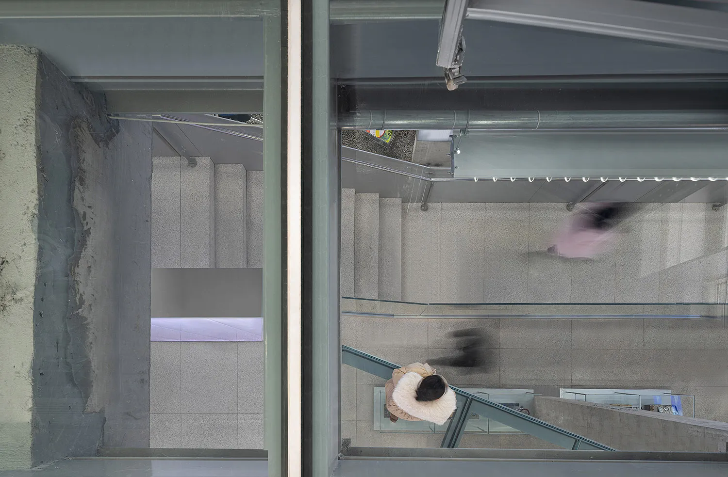 A top-down view of a modern urban concrete and glass walkway with blurred figures indicating movement.