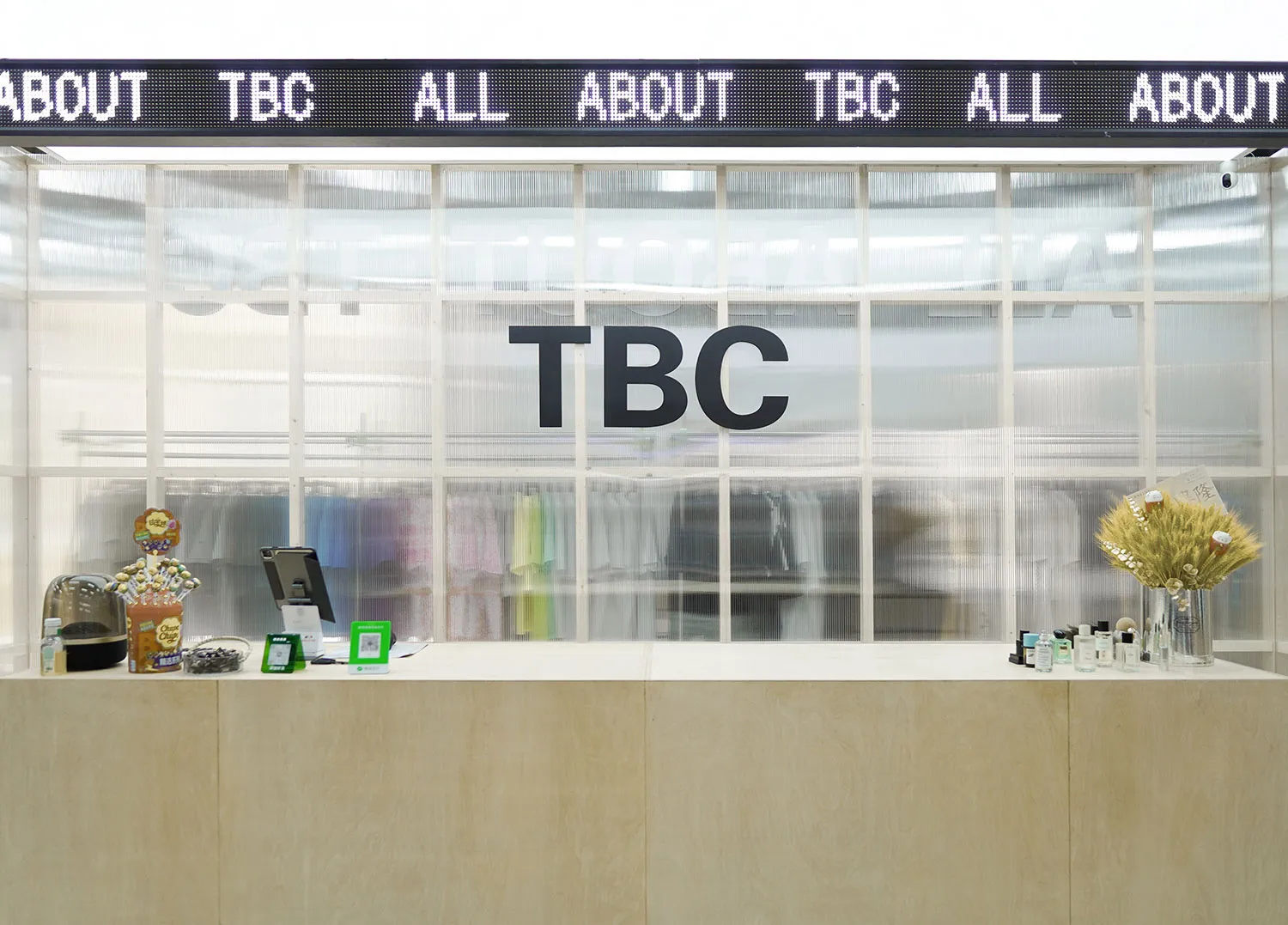 A contemporary reception counter made of wood, featuring a glass partition and a digital message board.
