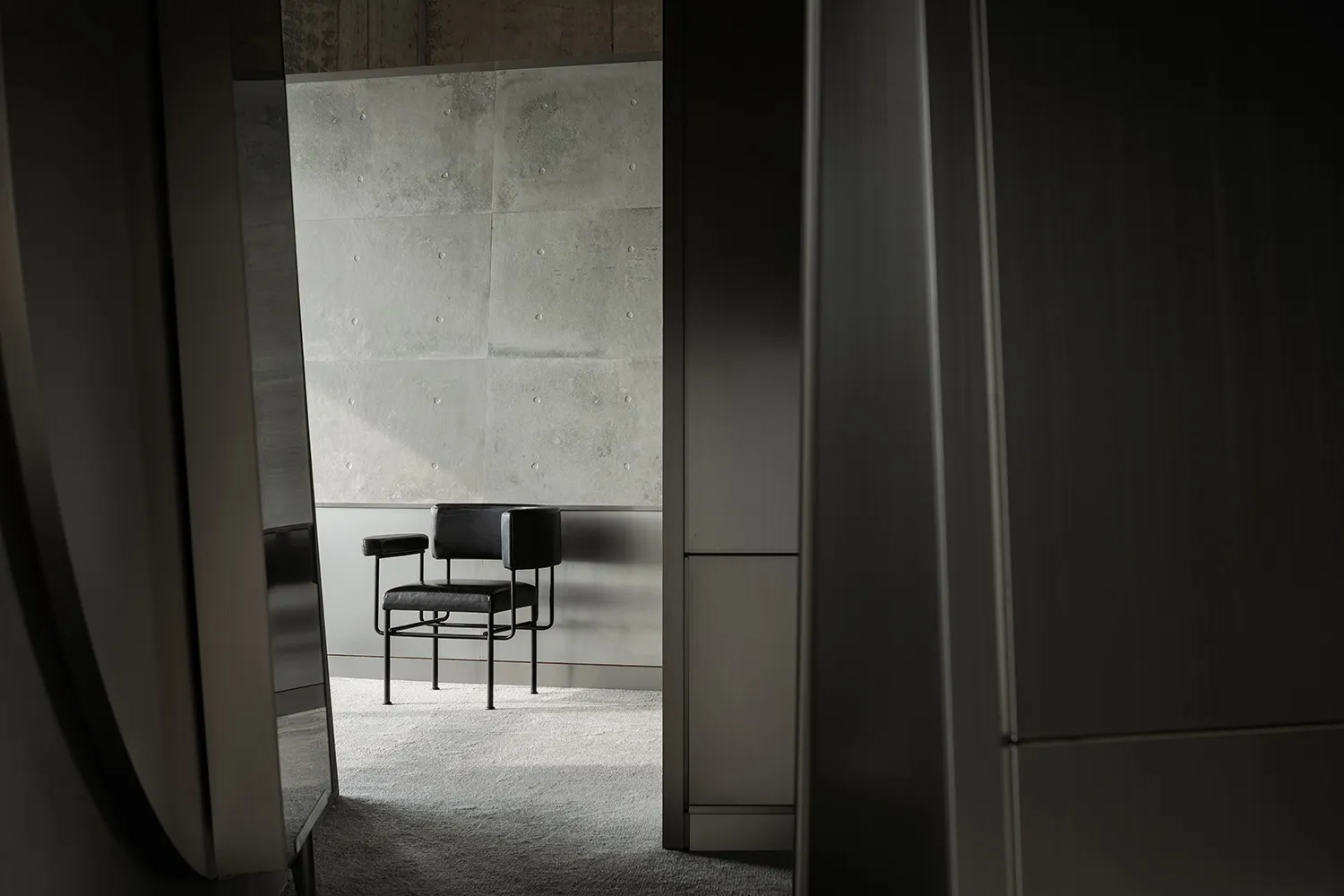 A modern interior with a concrete wall and a single black chair.