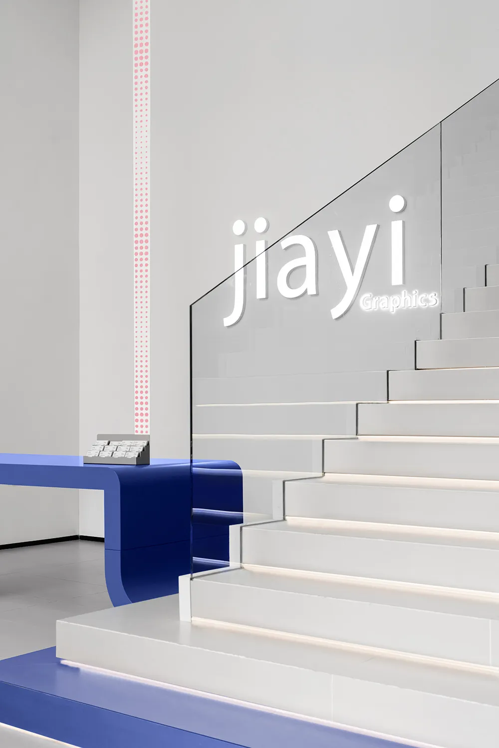 Modern office space featuring sleek white stairs with glass railings and a blue reception desk.