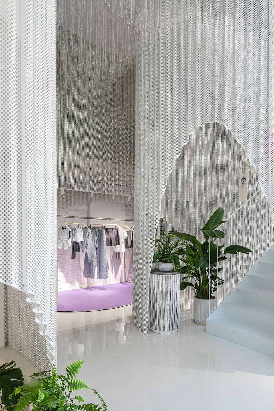 Modern retail store with a white interior, metal perforated screens, and green plants.