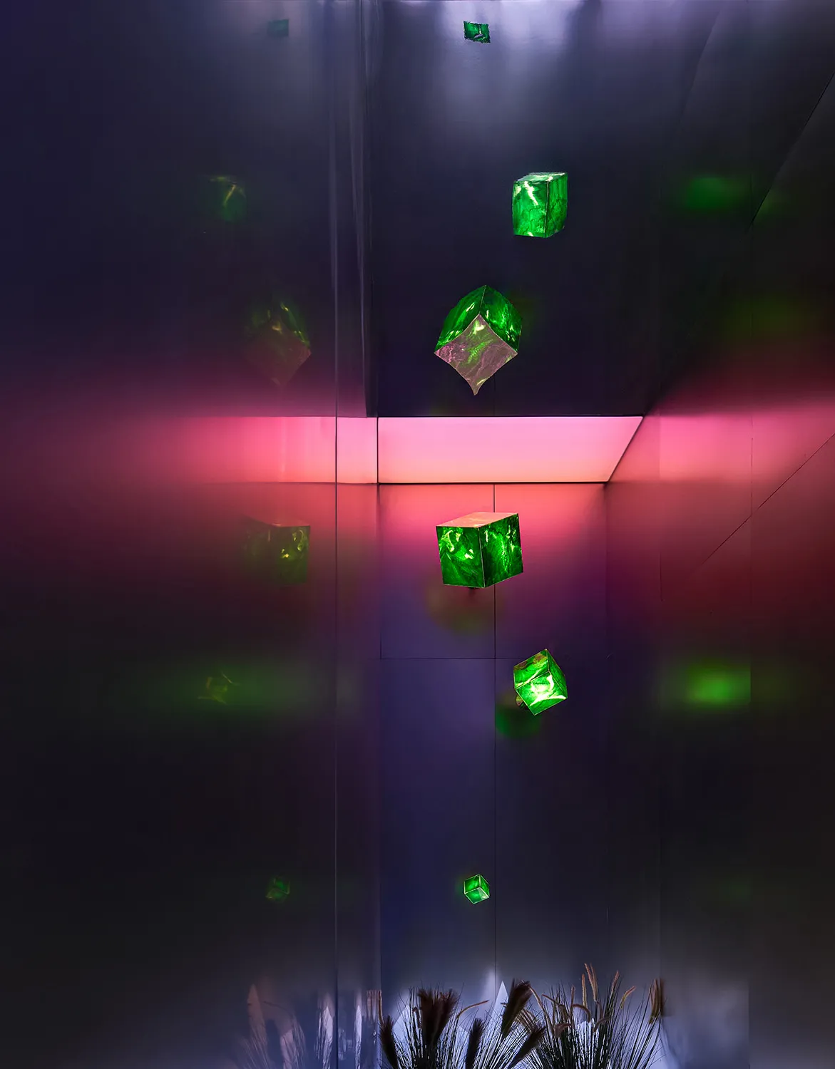 An abstract installation featuring green glass cubes suspended in a dark room with pink and purple lighting.