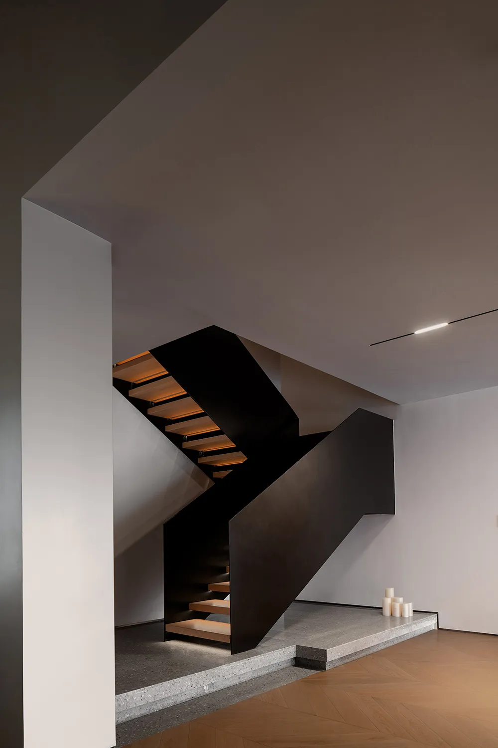 Modern staircase with black handrail and wooden steps illuminated by soft lighting.