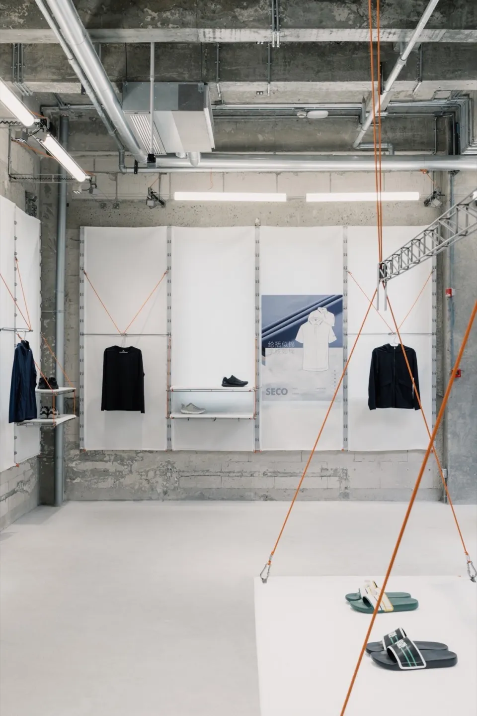 A retail display area with concrete walls, white shelving, and clothing items hanging.