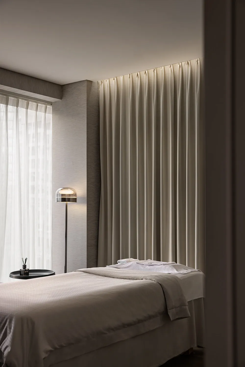 A minimalist bedroom featuring soft textiles, a neatly made bed, and a simple, elegant floor lamp.