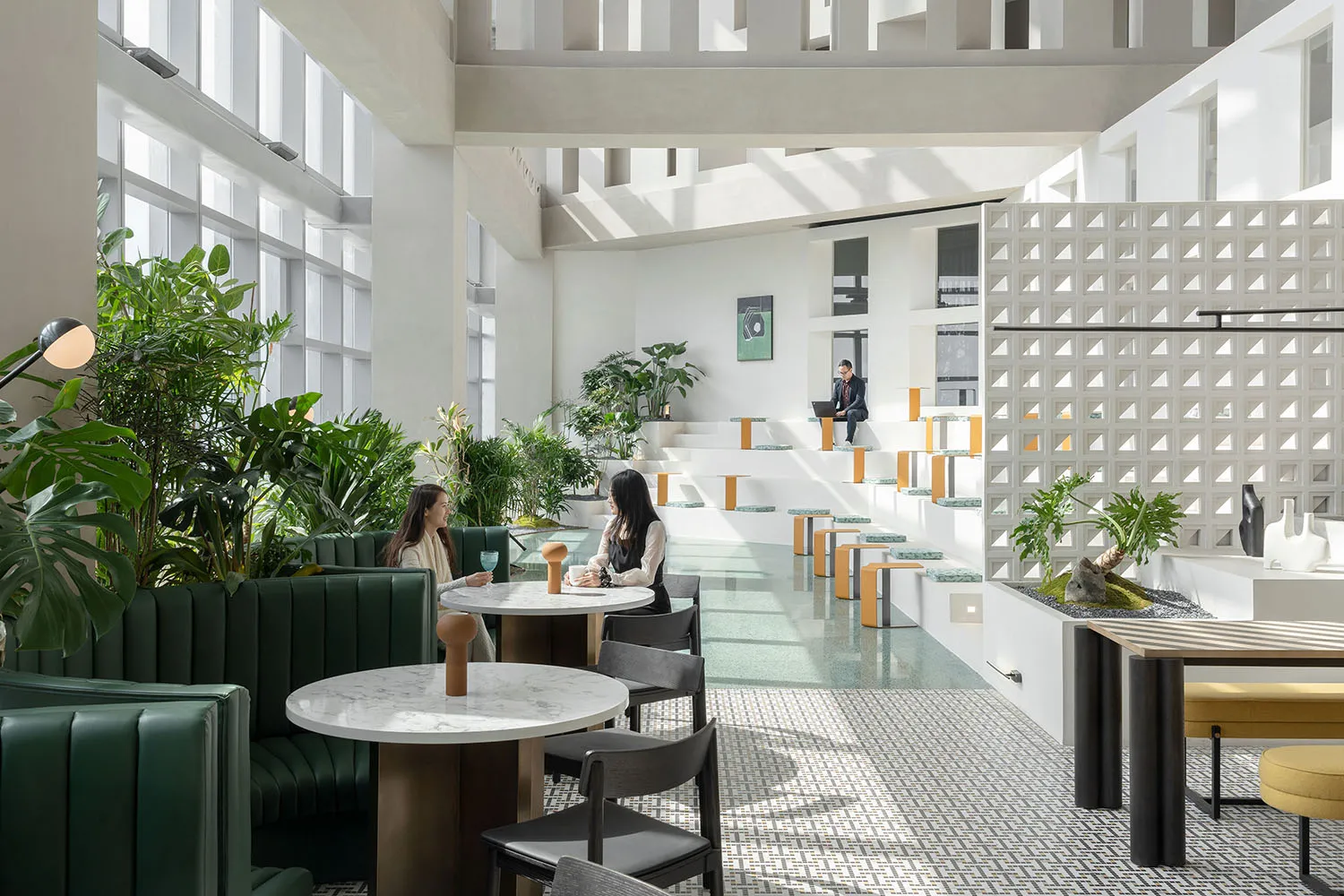 Modern cafe interior with green chairs, round marble tables, and plants.