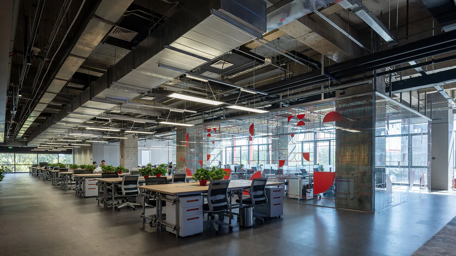 Industrial office space featuring concrete walls and floors, with exposed pipes and large windows.