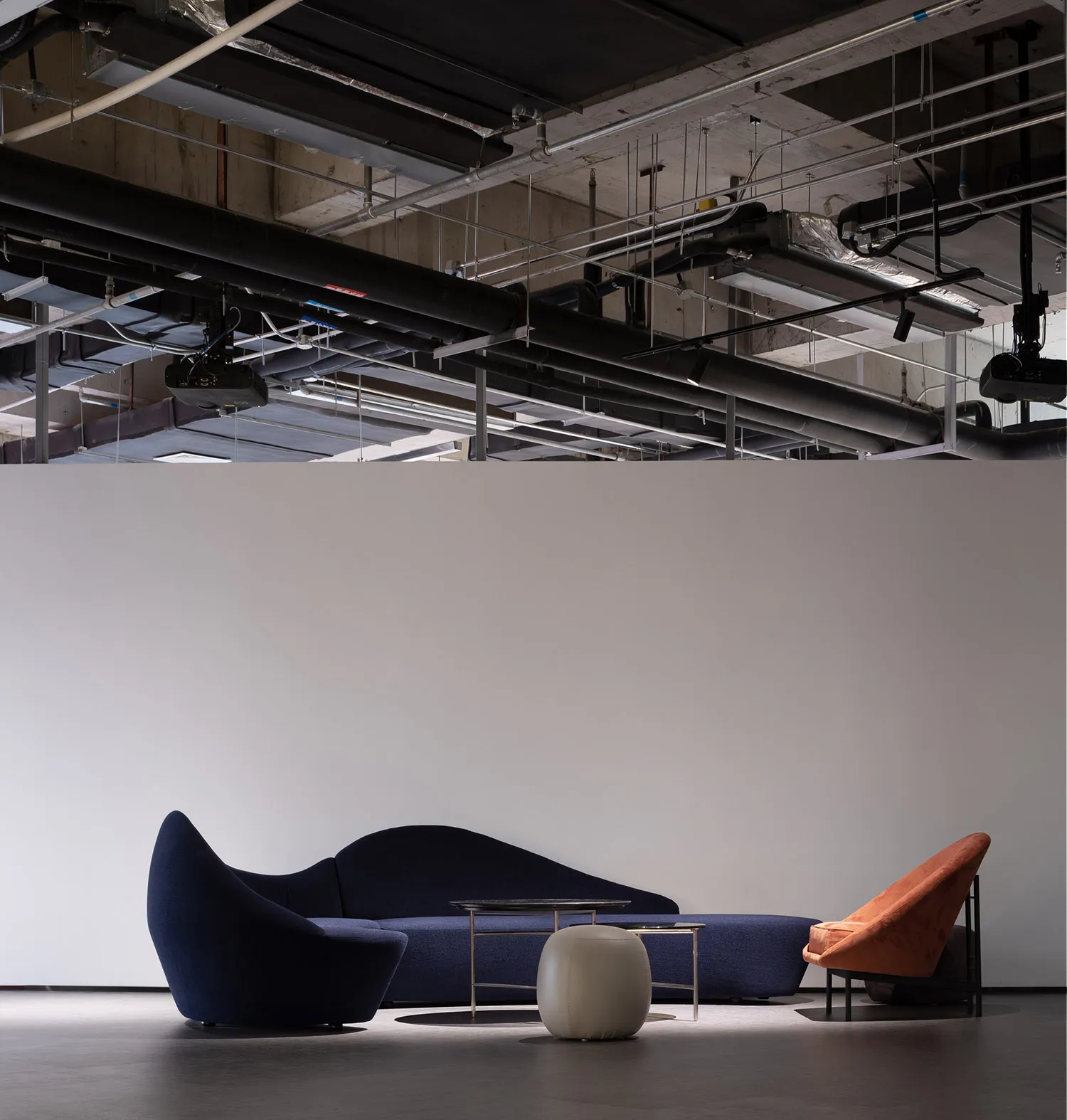 A modern lobby featuring a blue upholstered couch, an orange armchair, and a sleek metallic coffee table in front of a white