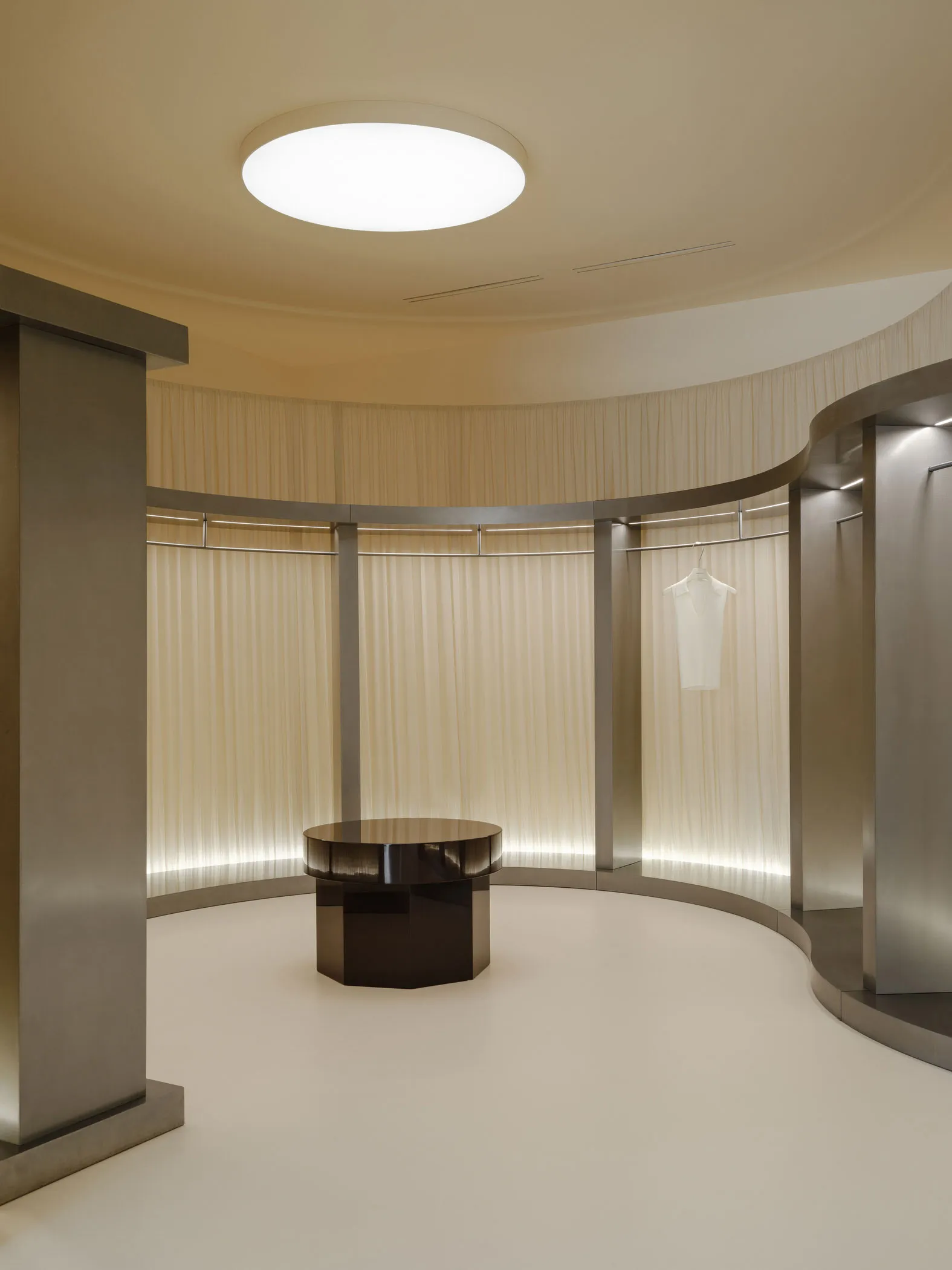 A minimalist fashion retail space with white fabric curtains, metal columns, and a white shirt hanging on a hanger.