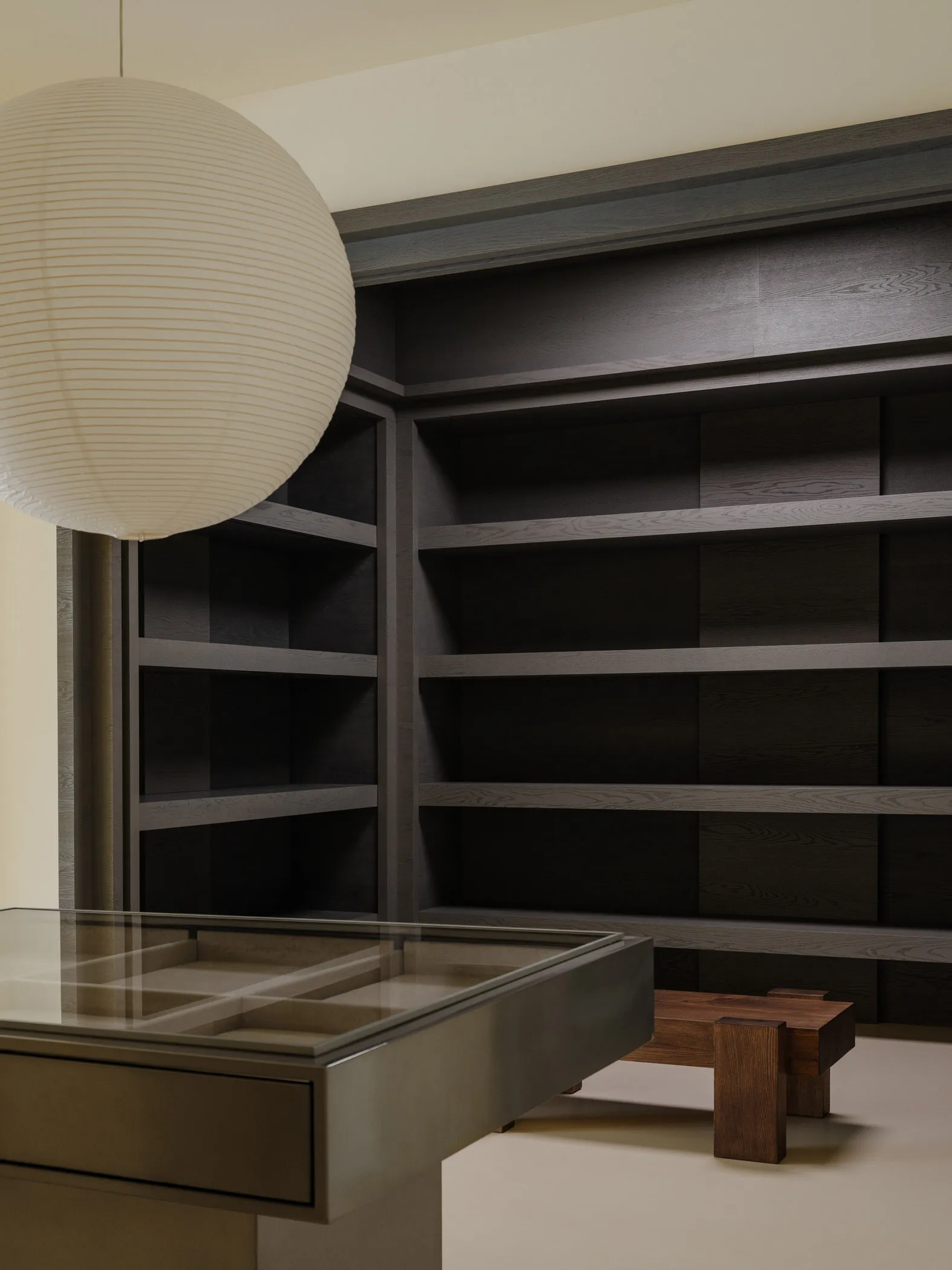A modern home library with dark wood shelves and a round paper lantern hanging above a glass-top table.