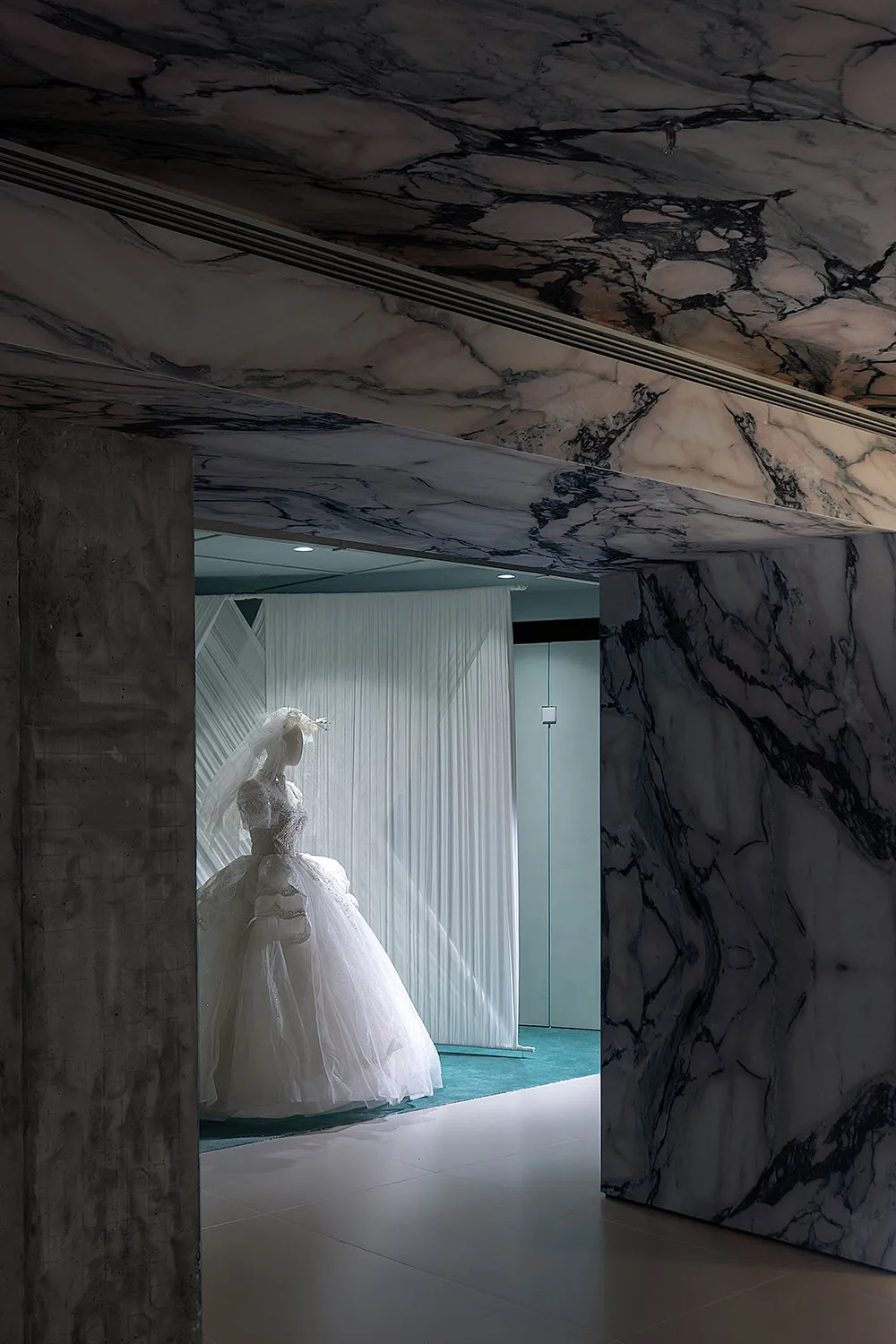 A display of a wedding dress within a room featuring marble and concrete architectural elements.