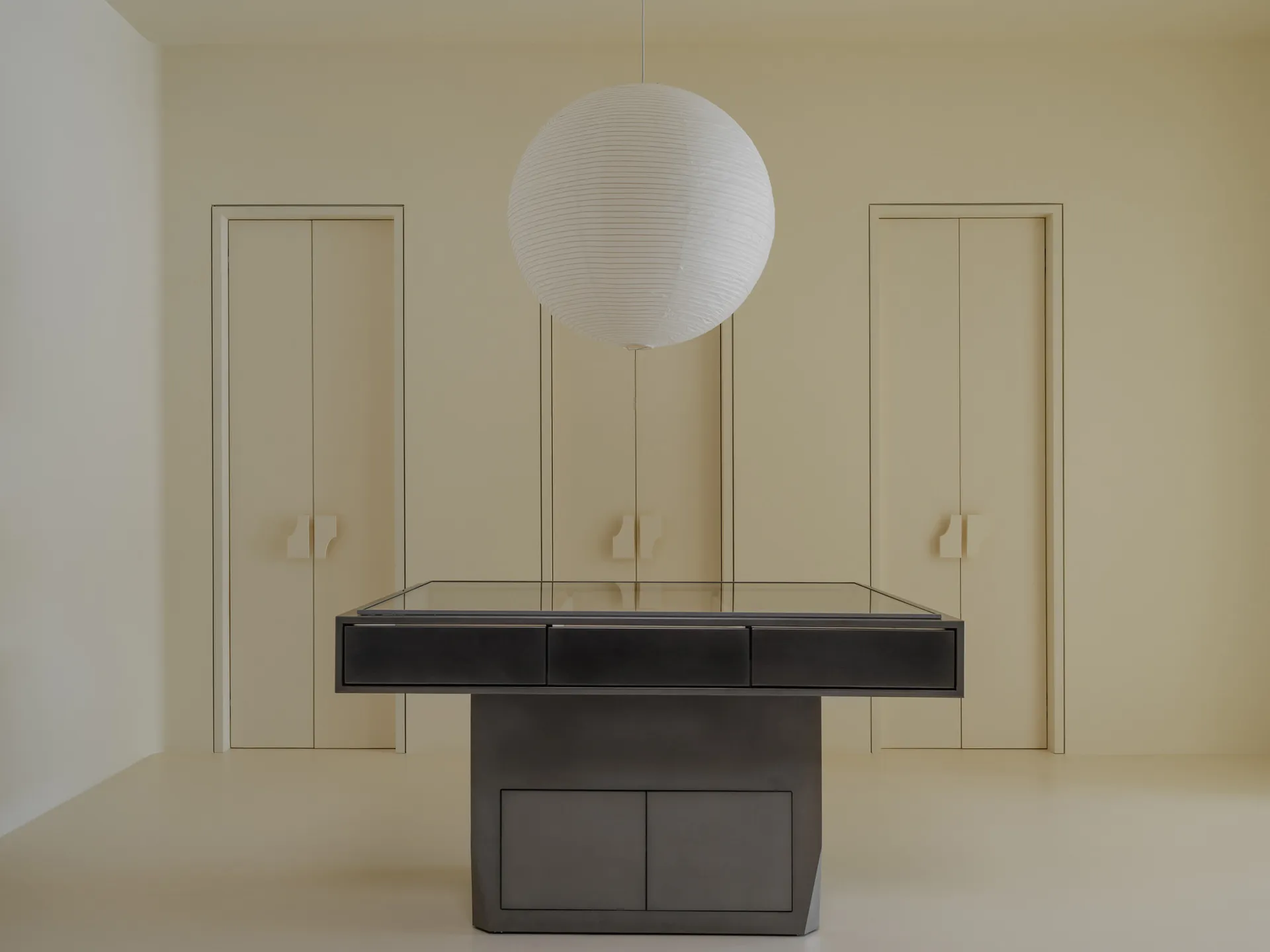 A minimalist black-and-white interior with a metal and glass table, white floor, and ceiling light.