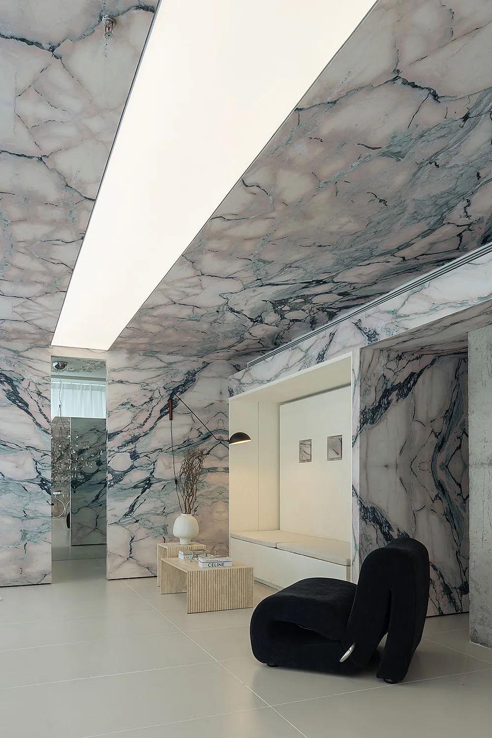 A contemporary living area featuring luxurious marble walls and ceiling, with sleek black furniture and minimalist decor.