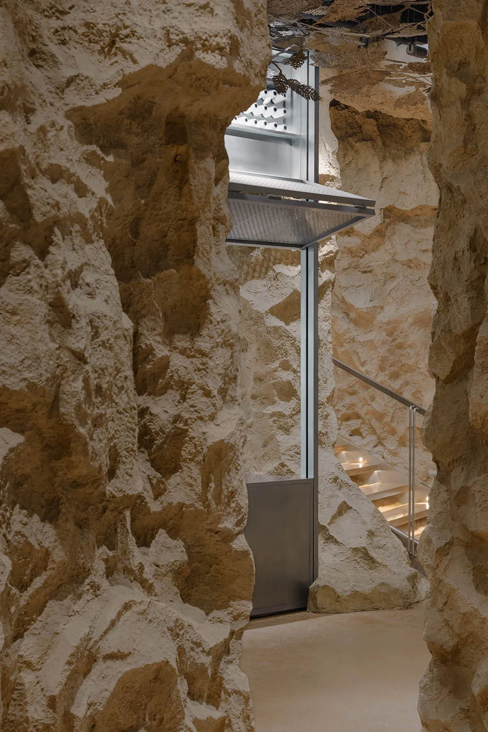 A modern, minimalist concrete reception area with a glass elevator lift and staircase.