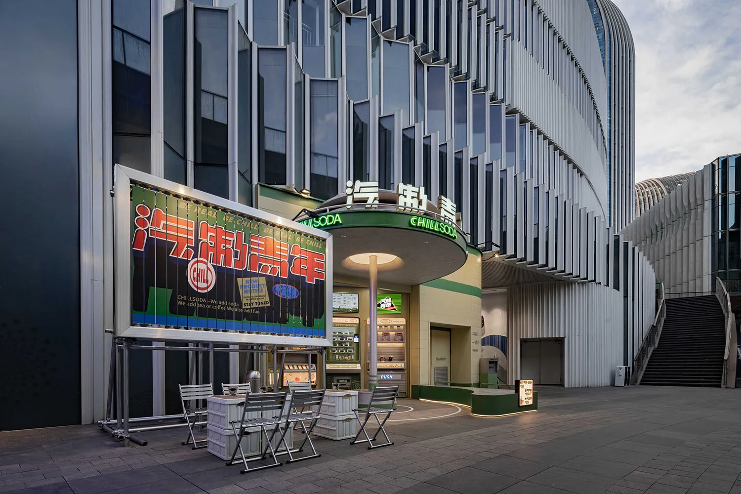 現代商業建築外觀採用金屬包覆與大面玻璃窗,搭配大型招牌及戶外座位區