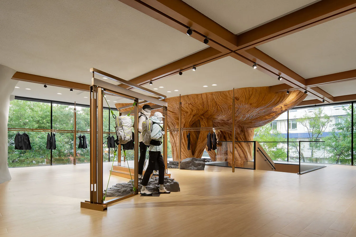 A modern retail storefront display featuring a large wooden tree trunk and mannequins with backpacks, set against a glass wal