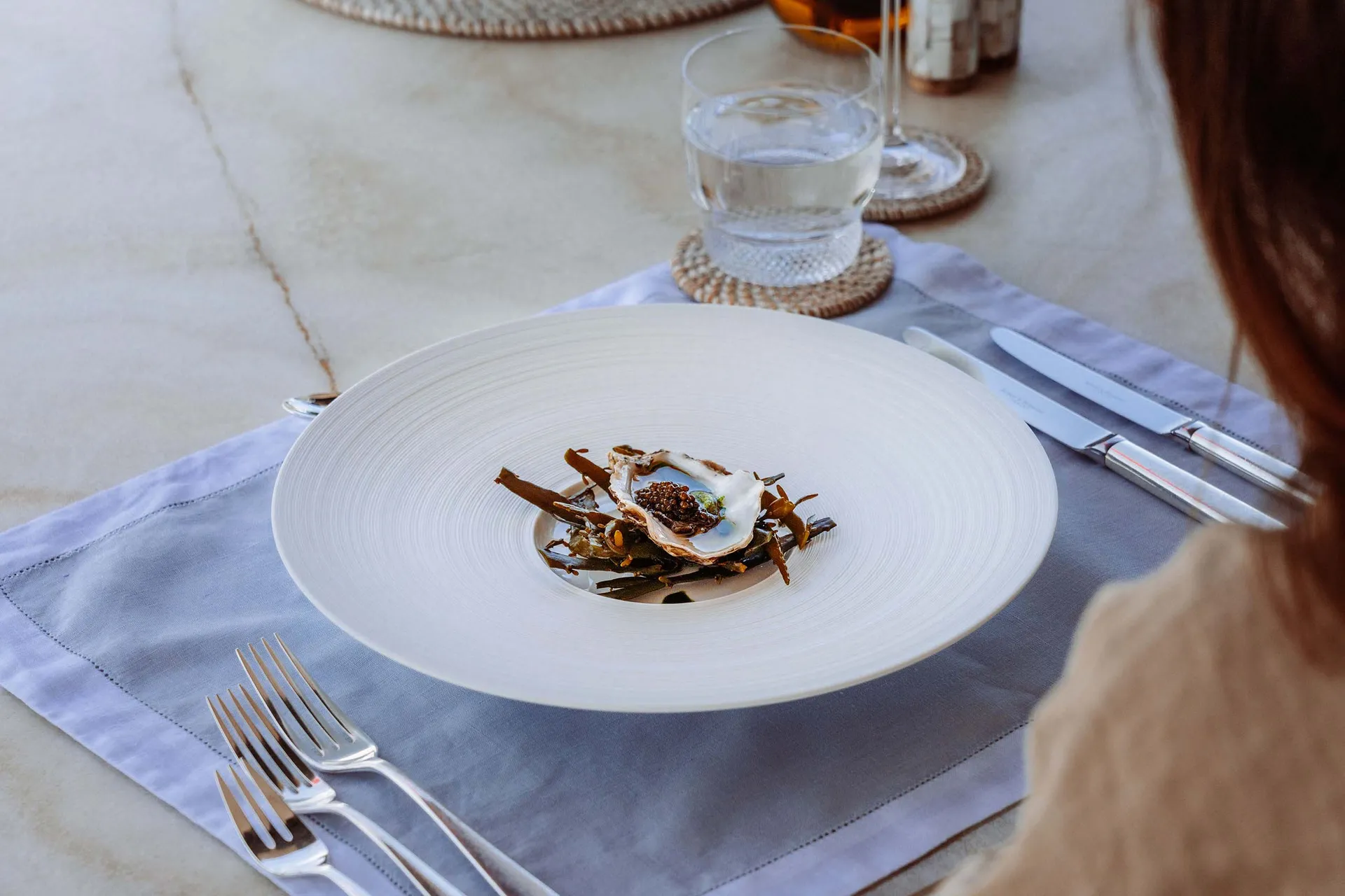 A white porcelain plate with a seafood dish, accompanied by a knife, fork, and a glass of water.