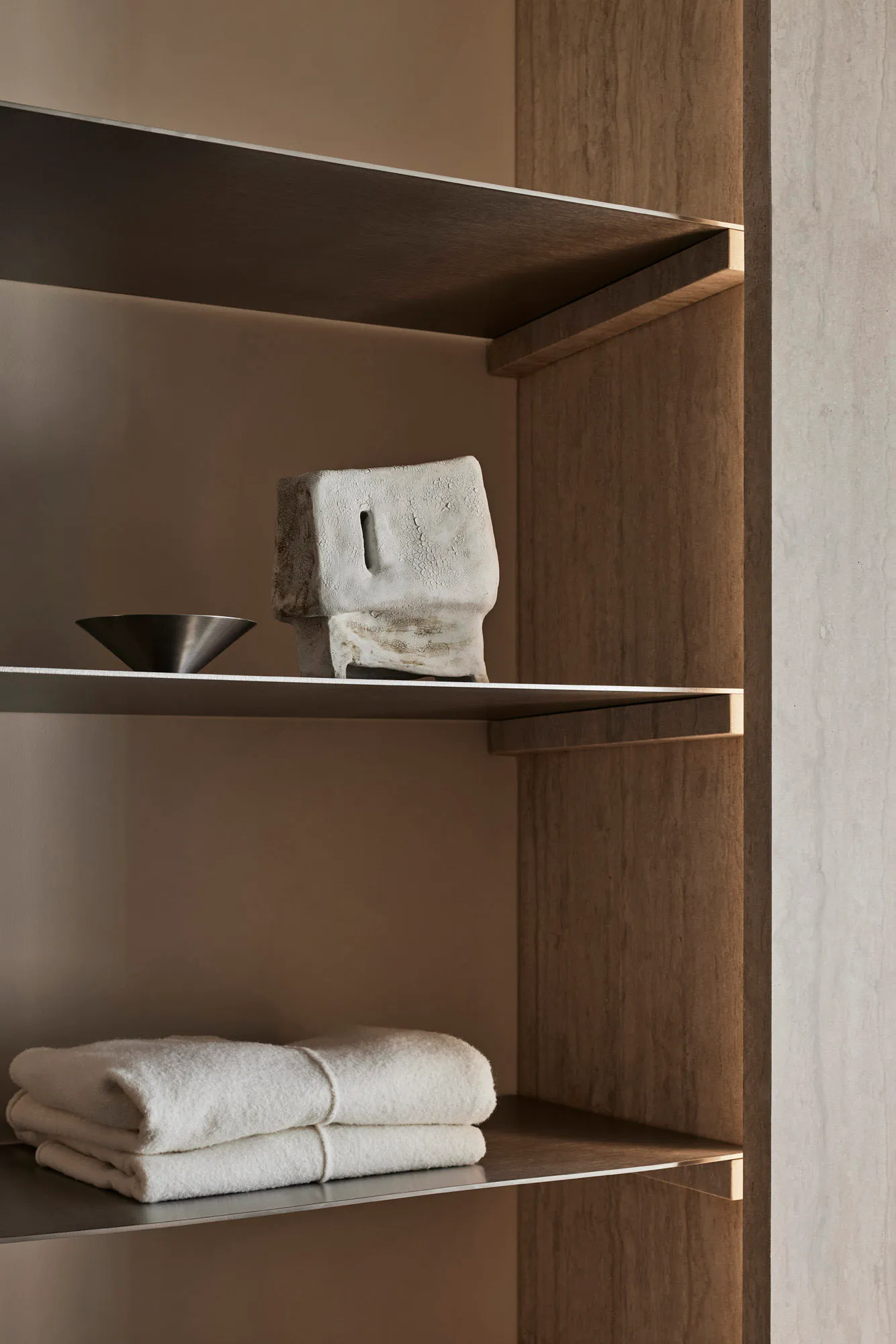 Metal shelves with wooden end supports holding white towels and a decorative stone object in a bathroom storage setting.