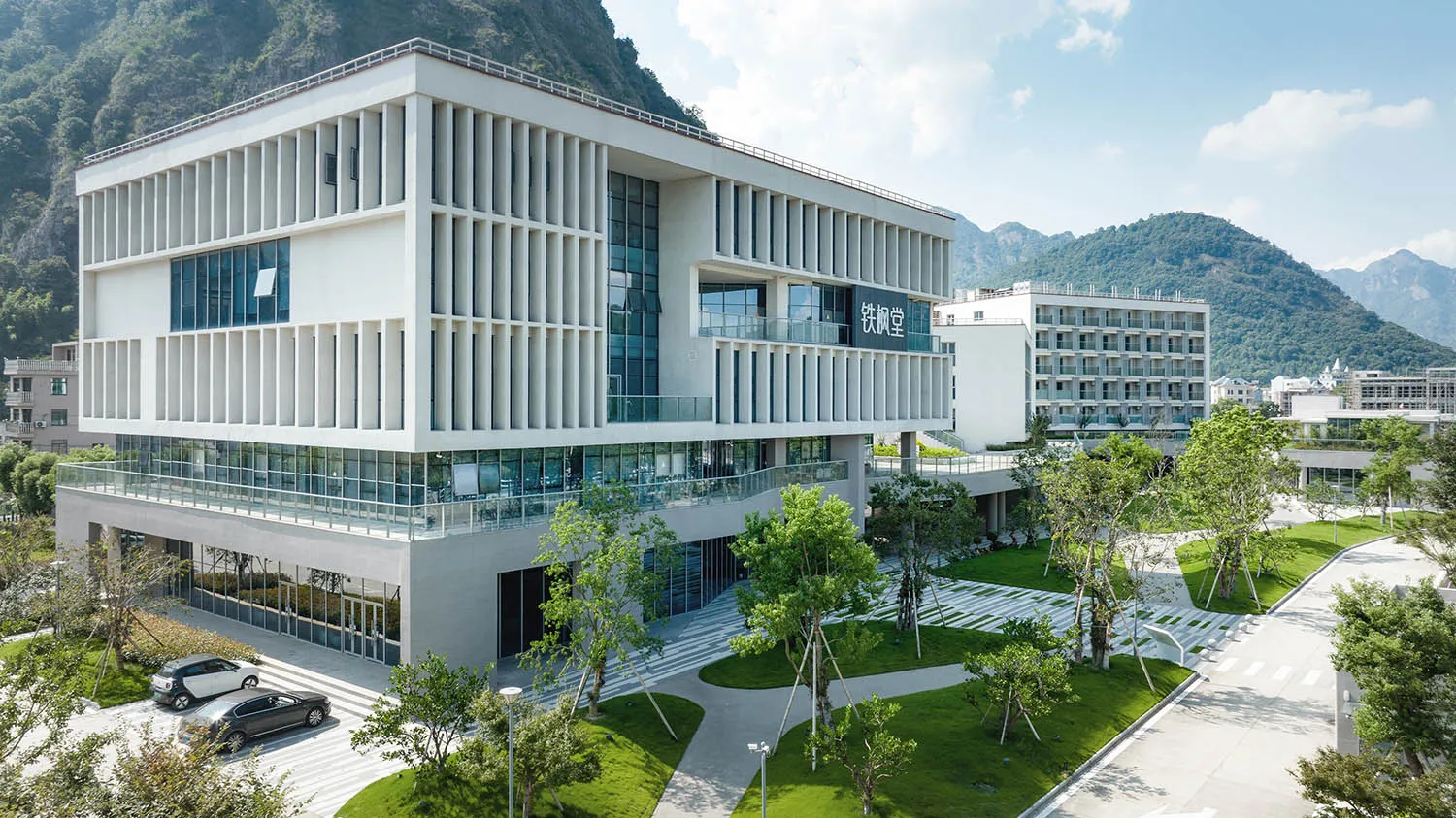 Modern office building with glass and concrete facades surrounded by greenery.