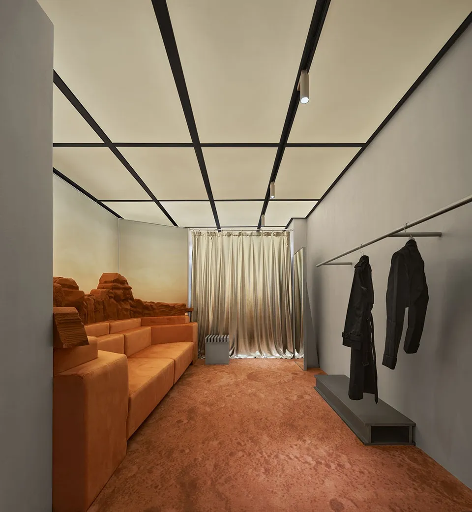 An industrial retail space with concrete walls, glass storefront, and seating area with orange sofas.