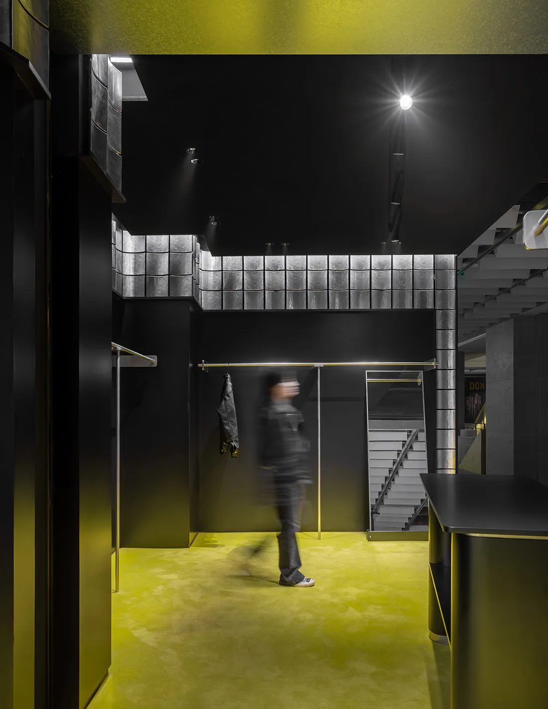 A modern retail store interior with metal tiles, concrete surfaces, and yellow accent lighting.