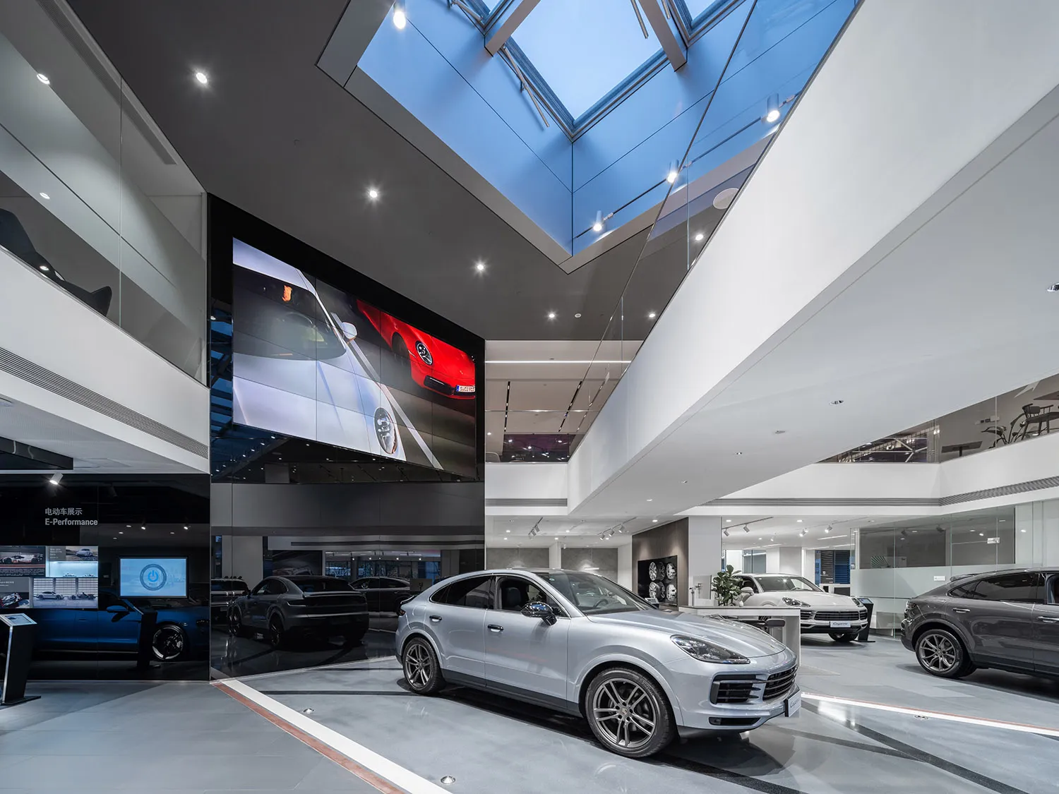 A modern car showroom with glass walls, polished concrete floors, and sleek car displays.
