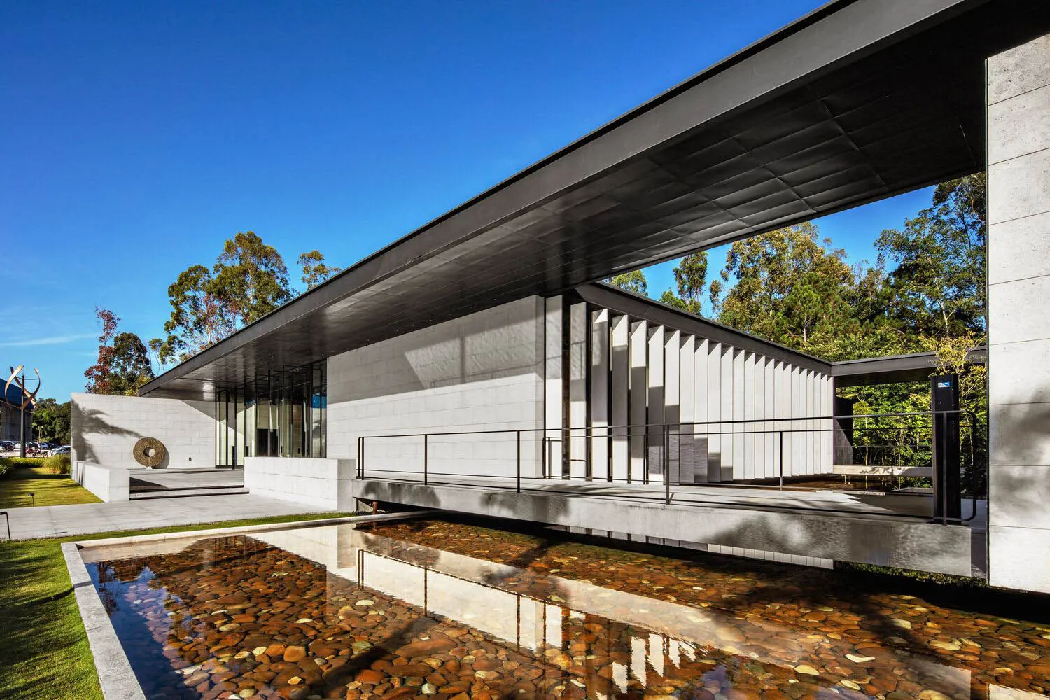 Modern exterior building made of concrete with a large overhanging roof and a reflecting pool with rocks.