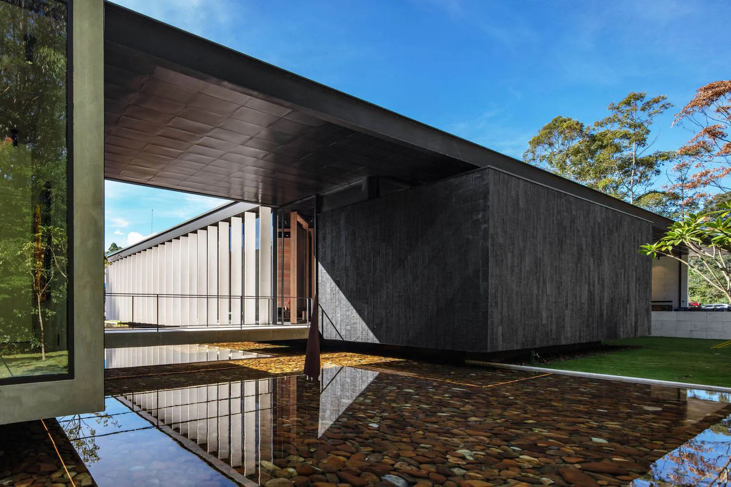 A modern house with a concrete and glass exterior reflected in a water feature.
