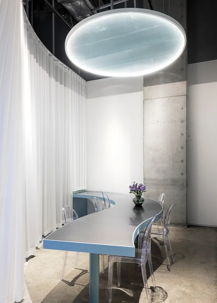 Luminous oval light fixture, white curtains, and glass chairs surround a sleek, modern conference room table.
