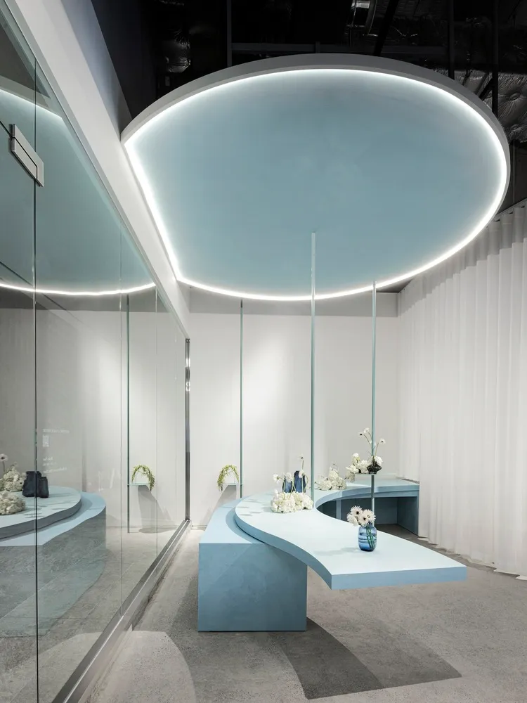 Minimalist retail store interior with blue concrete floor, matt white walls, and floral arrangements.