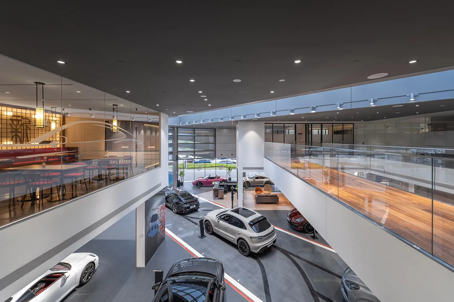 Modern, spacious car showroom featuring glass walls and metal accents, with a variety of luxury vehicles on display.