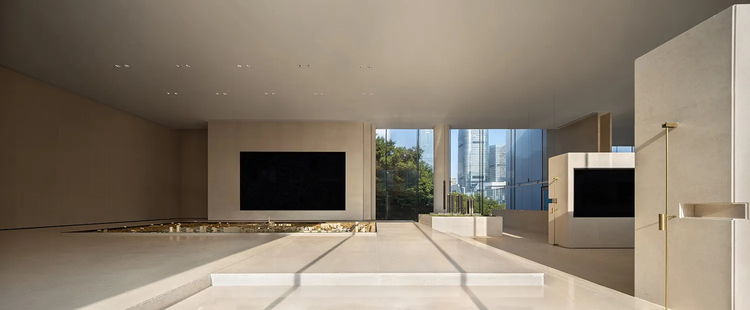 A spacious, minimalist lobby with concrete flooring, large windows, and a central screen.