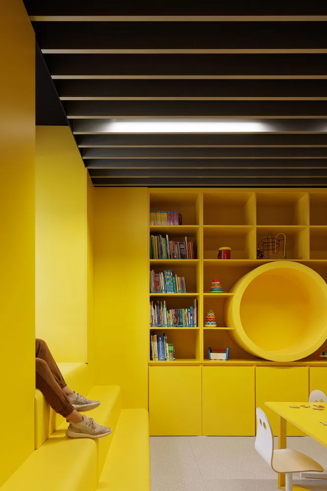 A brightly colored children's playroom with yellow furniture and shelves filled with toys and books.