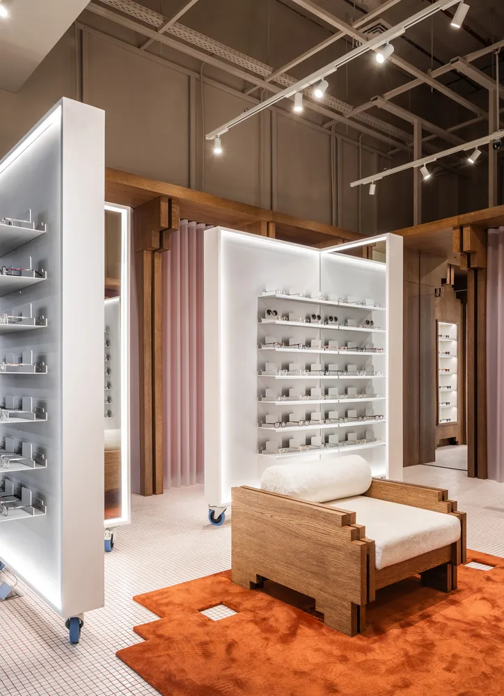 A modern retail display featuring a white panel with glass shelves and wooden armchair on a terracotta rug.