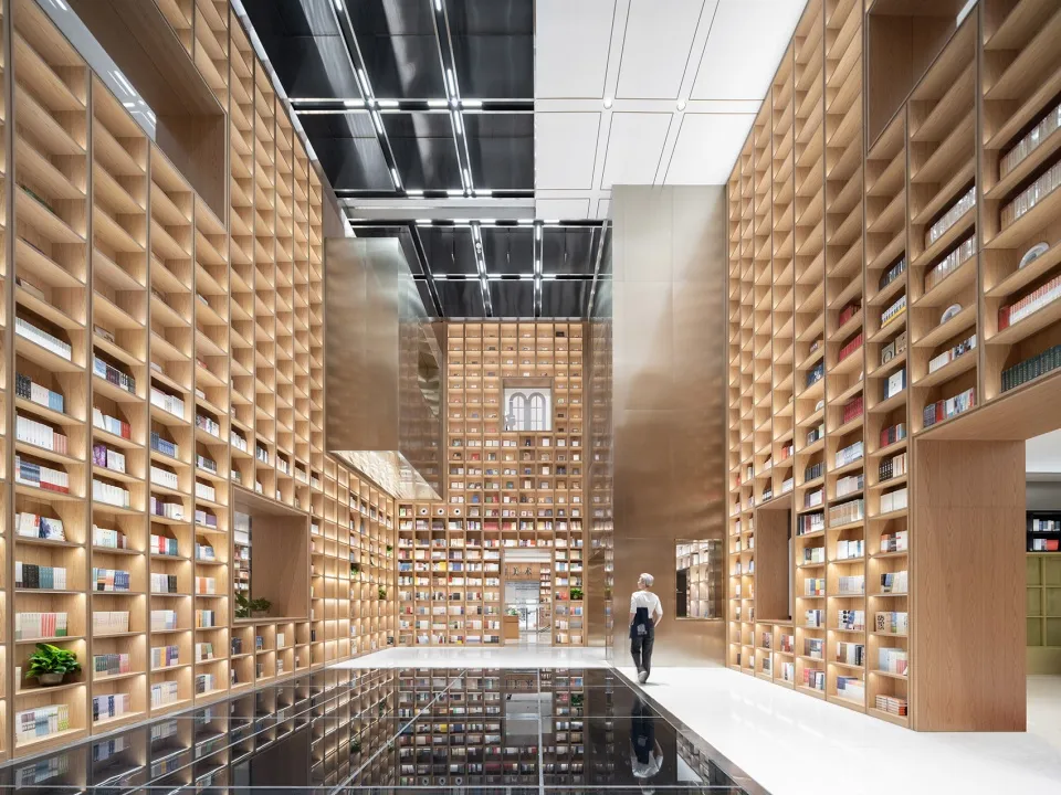 Library interior with minimalist design featuring wooden shelves and glass elements.