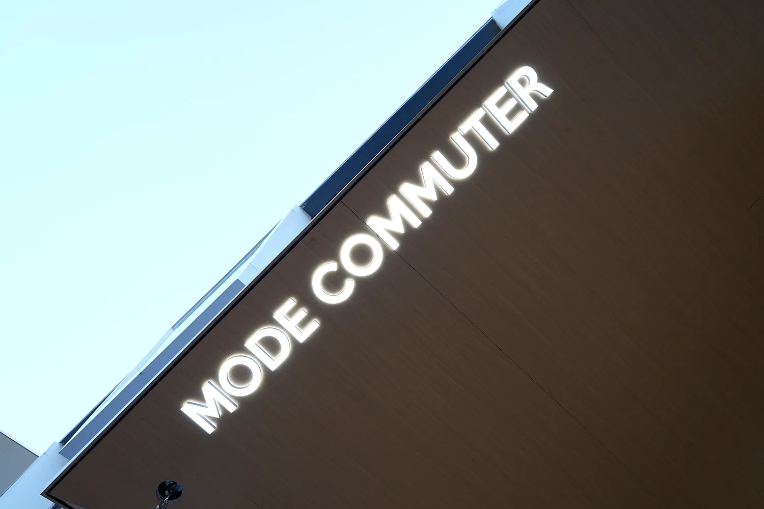 A lit-up metal sign with the words "MODE COMMUTER" mounted on a modern architectural structure.