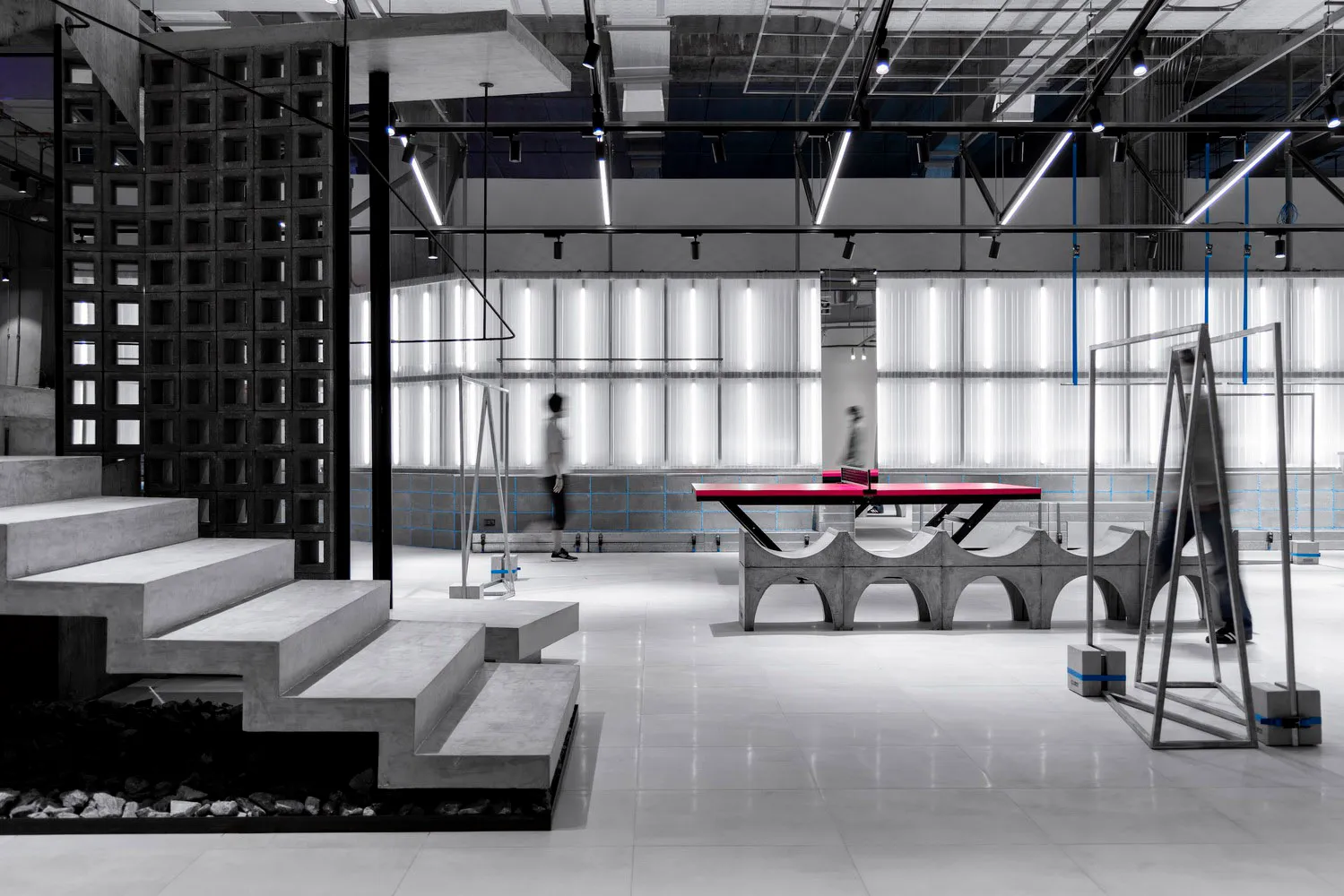 A spacious, modern sports gymnasium with concrete walls and a ping pong table.