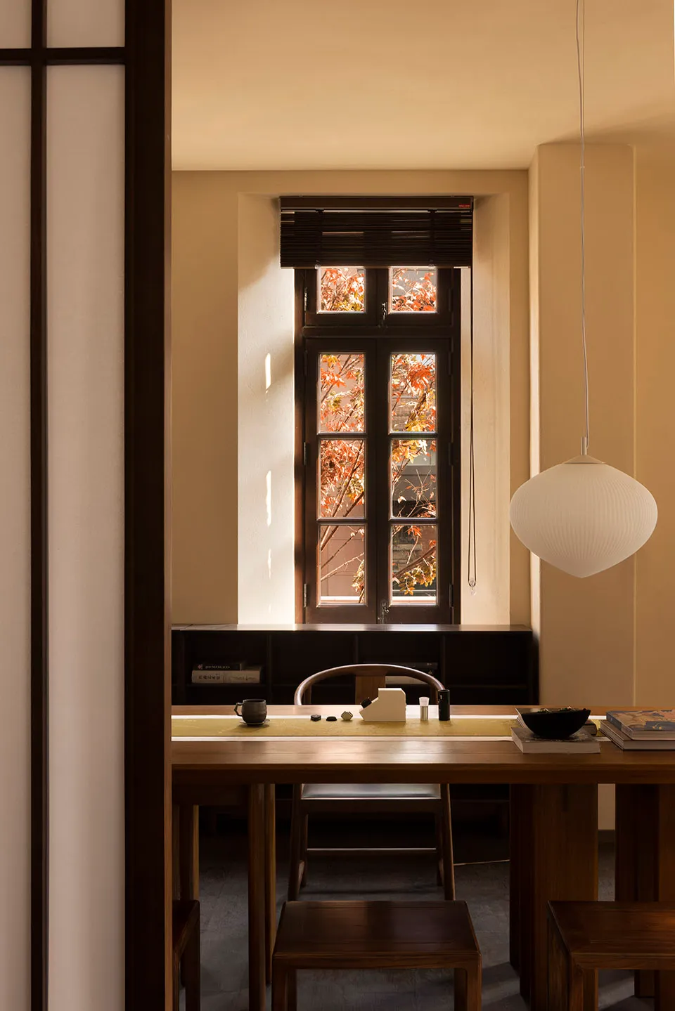 A modern residential interior featuring wooden furniture and a window with autumn leaves outside.